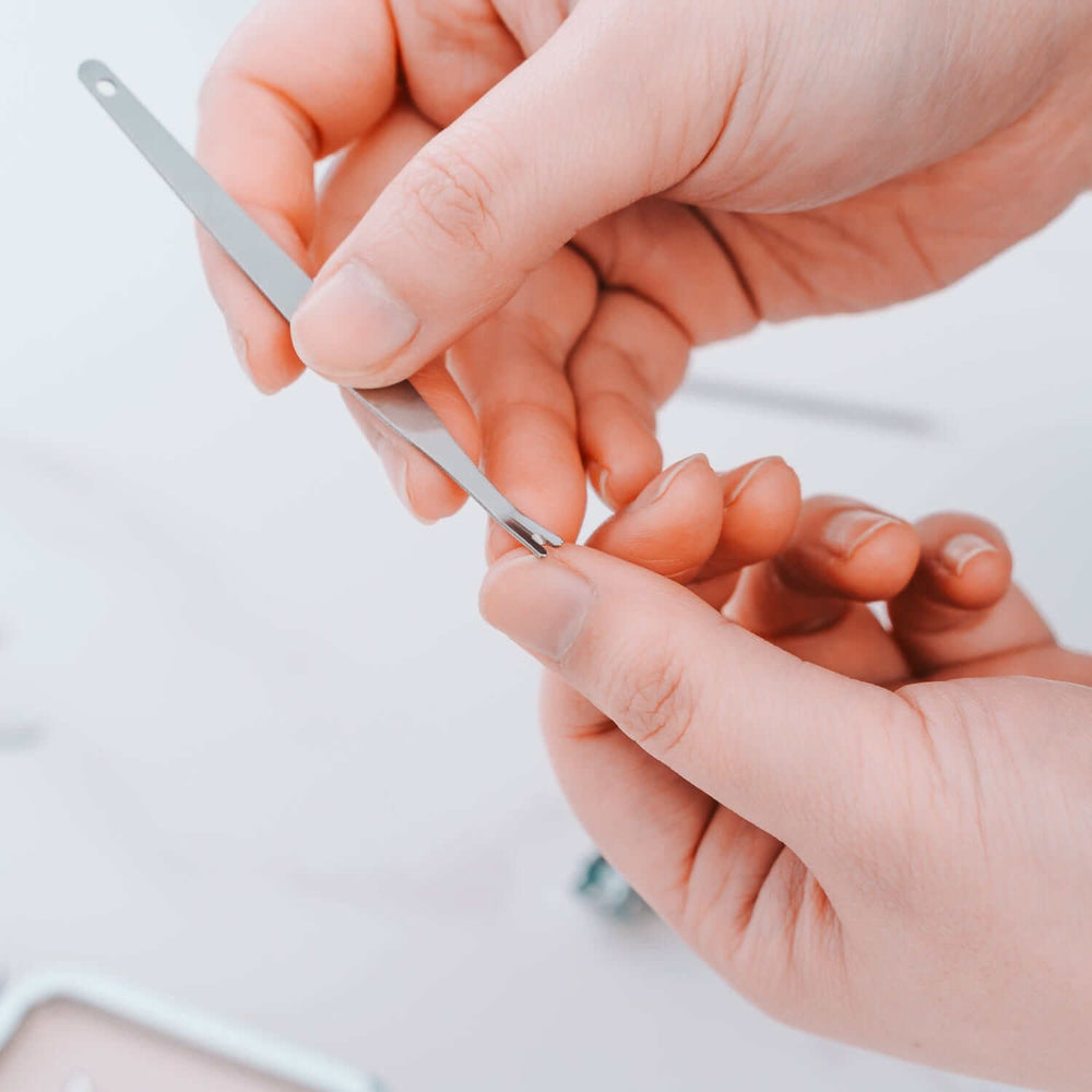 Close-up of hands using a stainless steel tool from the Remology 10pc manicure set for DIY nail care.