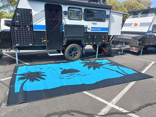 Spacious blue recycled poly camping mat with palm tree design under a camper trailer at a campsite.