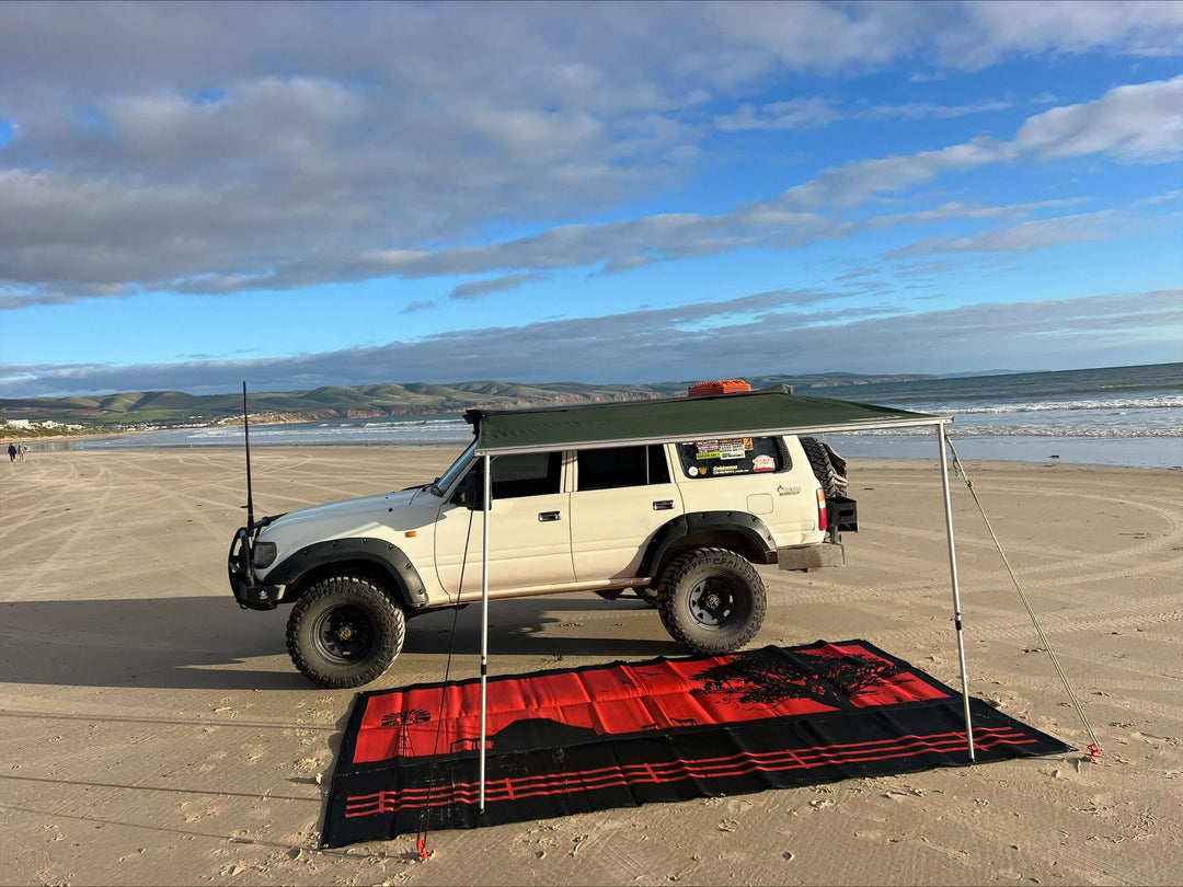 Off-road vehicle with awning on a sandy beach, showcasing the Country Orange recycled camping mat below.