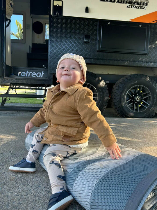 Toddler enjoying a cozy moment on a recycled poly camping mat outdoors next to a camper van.