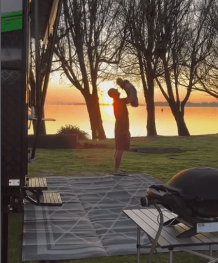 Person enjoying sunset outdoors with a camping mat and grill, showcasing a peaceful camping experience.