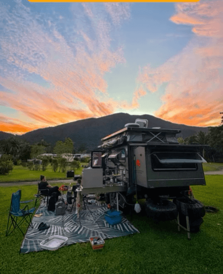 Scenic campsite at sunset with a camping mat set up in front of a van, showcasing outdoor relaxation and adventure.