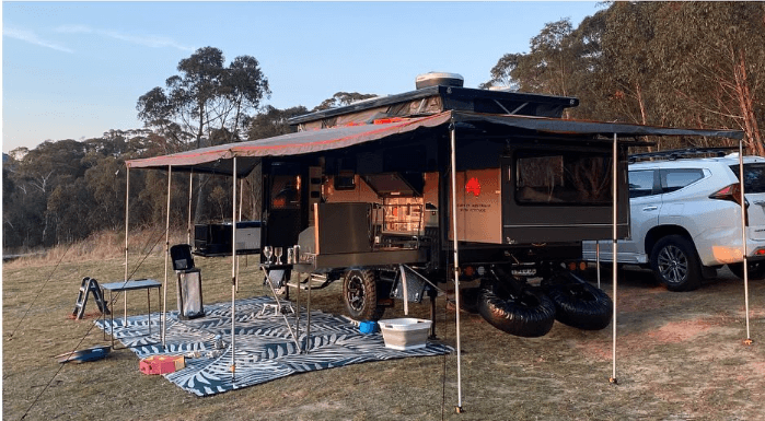 Camping setup with a trailer, 6m x 2.4m recycled poly mat, outdoor comforts, and beautiful natural surroundings.