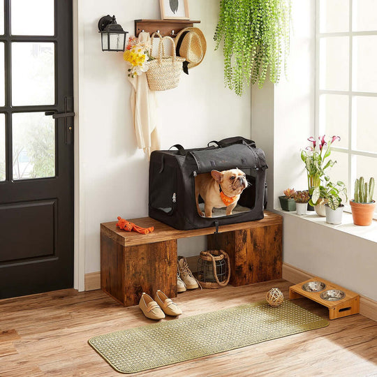 French Bulldog in black FEANDREA dog carrier on wooden bench near window, showcasing quality and affordable pet travel solution.