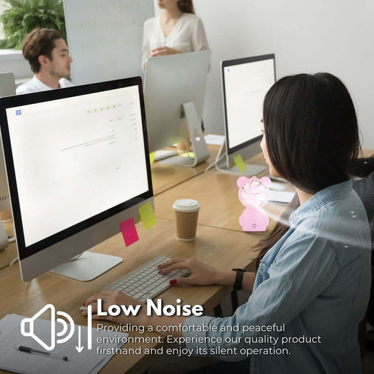 Woman working at a desk with a low noise handheld fan, promoting a peaceful office environment.