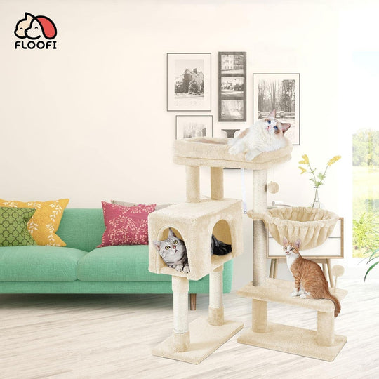 Cats playing on a multi-level beige cat tree in a modern living room with green couch and colorful cushions.