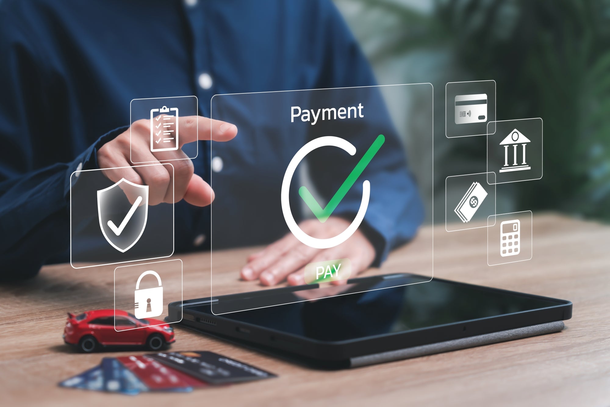 Person making an online payment on a laptop with digital payment icons and credit cards on the table.